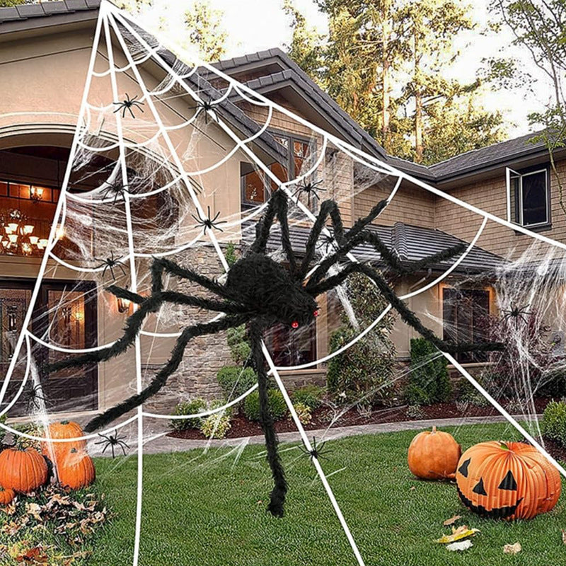 Halloween decorations including a large spider, cobwebs, and pumpkins in front of a house.